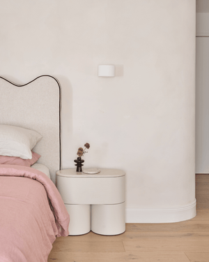 Blanco Interiors Project: A modern bedroom scene featuring a low, cylindrical nightstand with an up down plaster wall light.