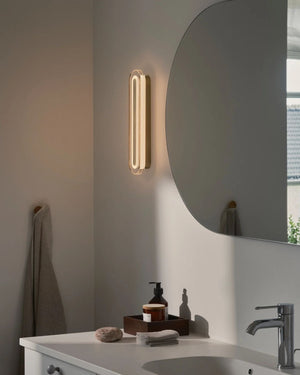 Art Deco Bathroom Wall Light in brass mounted vertically beside a round mirror above a bathroom vanity
