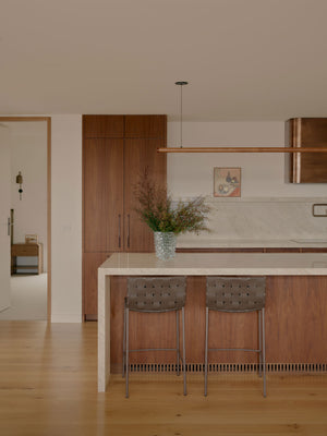 A modern kitchen interior with white marble, wood cabinetry and a timber linear pendant
