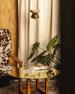 Round gold coffee table with a glass of water and a book, and a wooden dome pendant, in a dimly lit room.