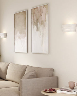 White ceramic three tier wall sconce installed above beige sofa beside abstract artwork