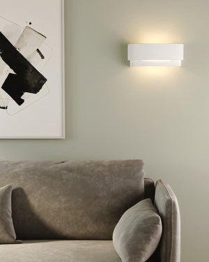 White ceramic two tier wall sconce installed above sofa beside black and white artwork