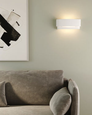White ceramic two tier wall sconce installed above sofa beside black and white artwork