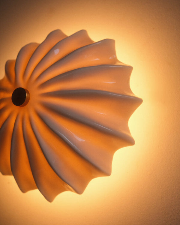 Close-up detail of white textured glazed ceramic wall sconce with warm light on