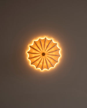 Small textured ceramic sconce hanging from white wall with warm light glowing