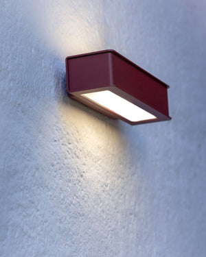 Wine red geometric wall sconce mounted on textured concrete wall casting upward and downward light