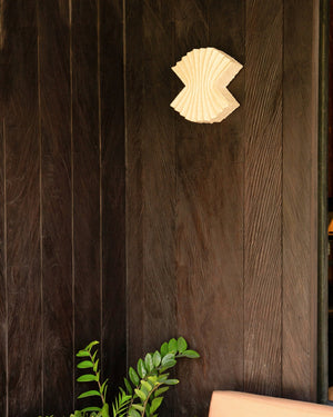 An off-white coastal pleat resin wall sconce mounted on a dark timber wall