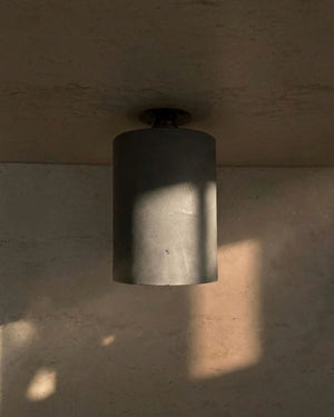 Concrete Cylindrical Downlight mounted on ceiling with dappled natural light and shadow across concrete walls