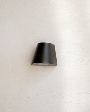 Conical indirect step light in antique brass mounted on a white textured wall