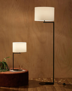Two floor lamps with white lampshades on a wooden surface against a wooden wall.