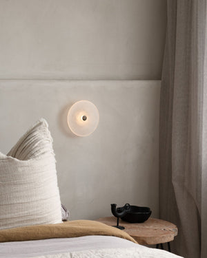 Wall-mounted light fixture on a neutral wall with a pillow and decorative item in the foreground.