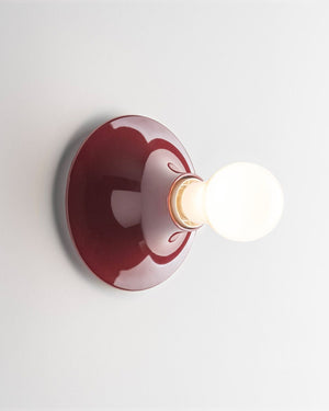 A modern wall-mounted light fixture with a round, glossy ruby red backplate and a white globe