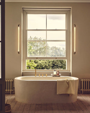 Modern bathroom with freestanding bathtub near a large window and Cylindrical Linear Bathroom Reeded Glass Wall Lights 