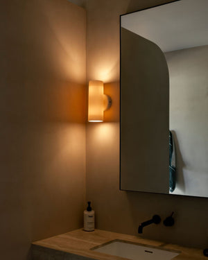 Bathroom corner with a mirror, white light fixture, and sink.