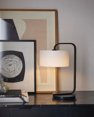 Modern table lamp on a dark surface with framed abstract art in the background.