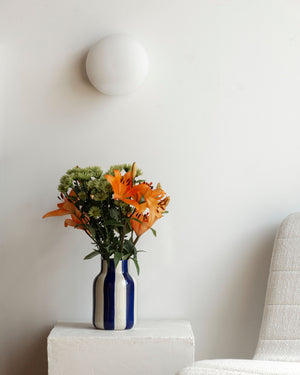 Flat glass disc ceiling light mounted above a vase with orange flowers