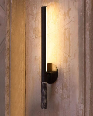 A modern vertical wall sconce with a copper cylindrical rod and a dark marble accent, shown against a textured beige wall