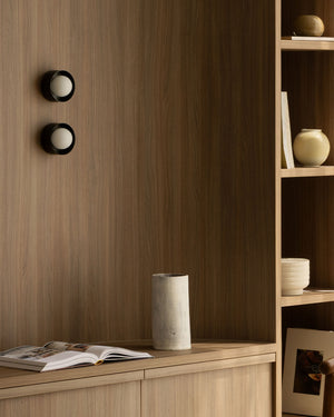 Wooden cabinet with an open book, a vase, and a small sculpture against a wooden wall.