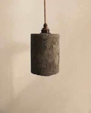 Hand cast concrete cylinder pendant with eroded surface texture hanging on jute cord with bronze fitting