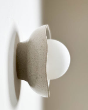 Shale glazed ceramic shell sconce with spherical bulb mounted on white wall side angle view