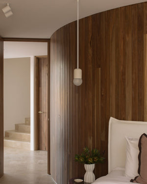 Modern bedroom with wood panelling and cylindrical pendant light installed above bedside table