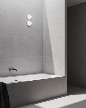Modern bathroom with a white bathtub against grey tiled walls, glass wall light