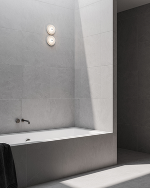 Modern bathroom with a white bathtub against grey tiled walls, glass wall light