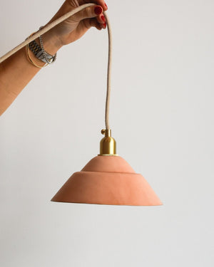 Hand holding up a leather shade pendant light in natural with a brass fixture