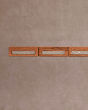 Mid-Century linear pendant light with rectangular wood-grain shades containing textured clear glass panes, suspended against a warm wall