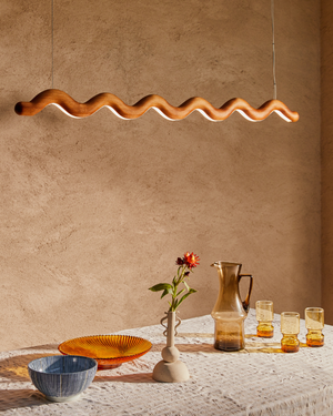Wavy pendant light fixture above a dining table with ceramic plates, glasses, and a vase.