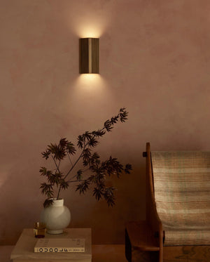 Wall-mounted light fixture casting a warm glow on a wall with a vase and plant on a table.