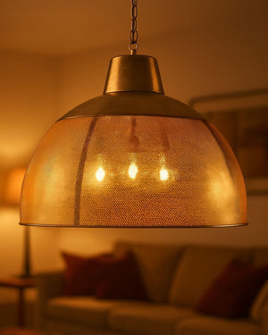A warm brass dome pendant light with a textured mesh shade, hanging in a cozy, living room