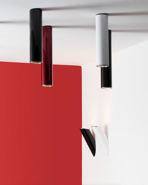 Modern cylindrical ceiling lights in black, dark red, white, and black, shown against a white wall and ceiling with a bold red geometric backdrop.