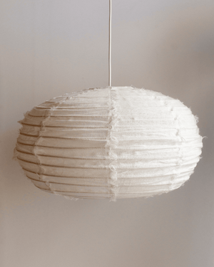 A white textured fabric paper lantern pendant light hanging from a thin white cord against a neutral beige wall.