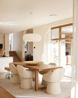 Three Birds House 18 Project - Maison Soleil: A modern dining room featuring a light oak wood dining table surrounded by six sculptural, upholstered cream chairs - with a large, ribbed white pendant light suspended over the table.