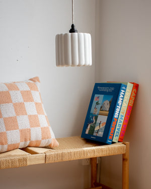Wicker bench with checkered pillow and books against a white wall with a pendant light.