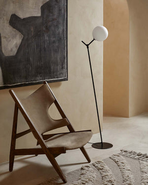 Modern floor lamp next to a wooden chair in a minimalistic room with abstract art on the wall.