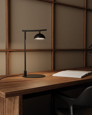 Modern black desk lamp on a wooden desk with a minimalistic background