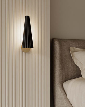Modern wall sconce on a textured wall next to a bed with pillows.