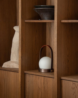 White spherical lamp with bronze base on a wooden shelf