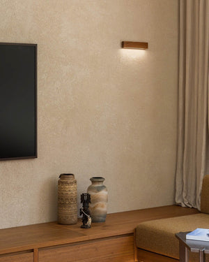 A modern rectangular wall sconce with a warm wood finish on a textured beige wall