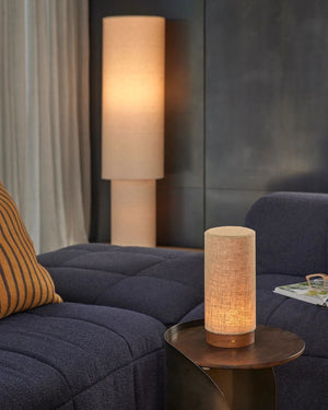 Linen drum table lamp illuminated on brass side table beside navy sofa in contemporary living room