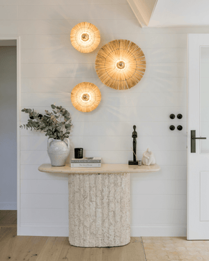 A-Frame Project: Three woven hay wall light fixtures in varying sizes styled above a textured stone console table
