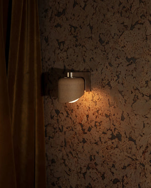 Wall-mounted light fixture on a textured wall with a curtain to the left.