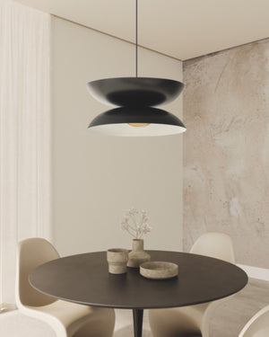 Minimalist Double Disc Pendant in matt black suspended above round dining table in minimalist interior with stone wall