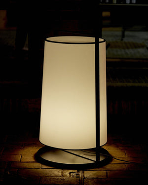 White cylindrical lamp with black metal frame on a dark background