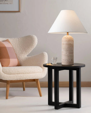 Travertine base table lamp with linen shade on a black side table in a modern living room