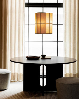 Modern black dining table with a lamp and decor items in a room with large windows and curtains.
