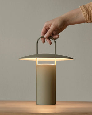 Hand holding a modern green table lamp against a neutral background
