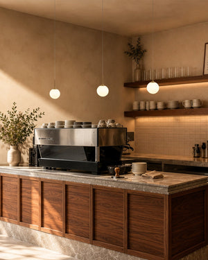 A modern cafe setting with wooden cabinets, hanging pendant lights, and shelves in the background.